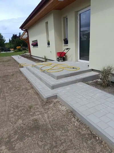 Vstupní schody a chodník ze světle šedé dlažby u nového rodinného domu