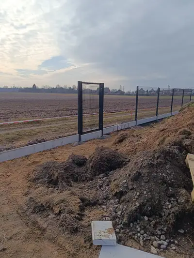 Panelový plot s brankou a podhrabovými deskami na kraji pole