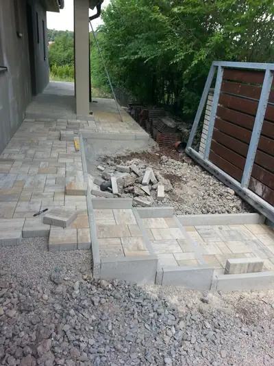 Rozpracovaný chodník z dlažby podél domu se štěrkovým podkladem