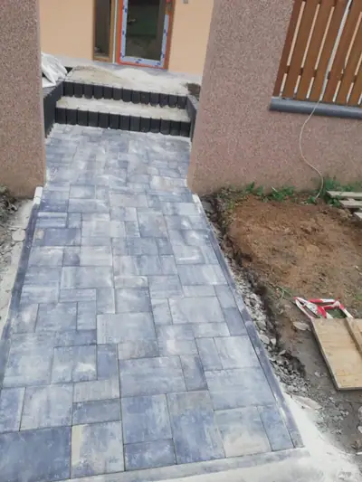Chodník ze šedomodré dlažby mezi domy, nahoře tmavé schody