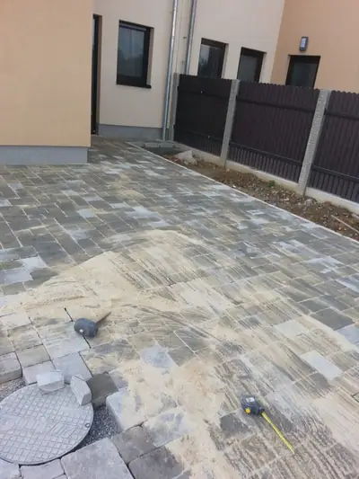 Dlažba v šedém melíru podél domu při zametání písku do spár