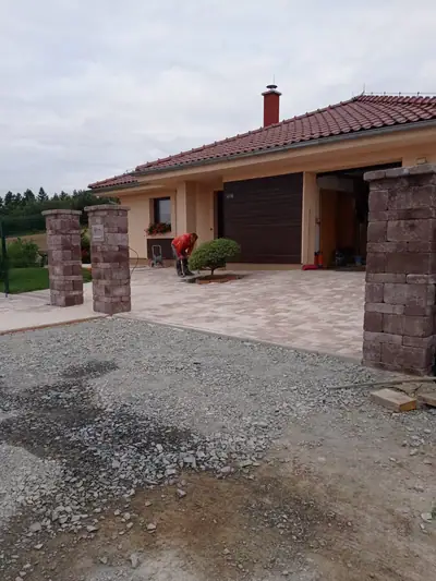Vjezd ze světle cihlové dlažby mezi sloupky ze štípaných tvárnic