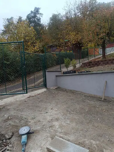 Zelená branka a pletivový plot nad omítnutou opěrnou zídkou, před úpravou terénu
