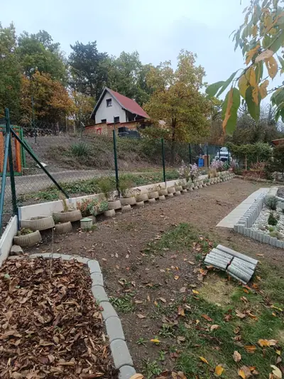 Zahrada s obrubou záhonů z betonových obrubníků a palisád, nahoře pletivový plot